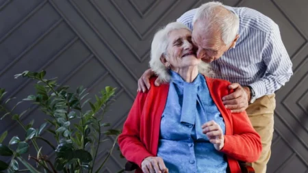 Älteres Ehepaar sitzt im Garten, Mann gibt Frau einen Kuss und die Frau lächelt zufrieden