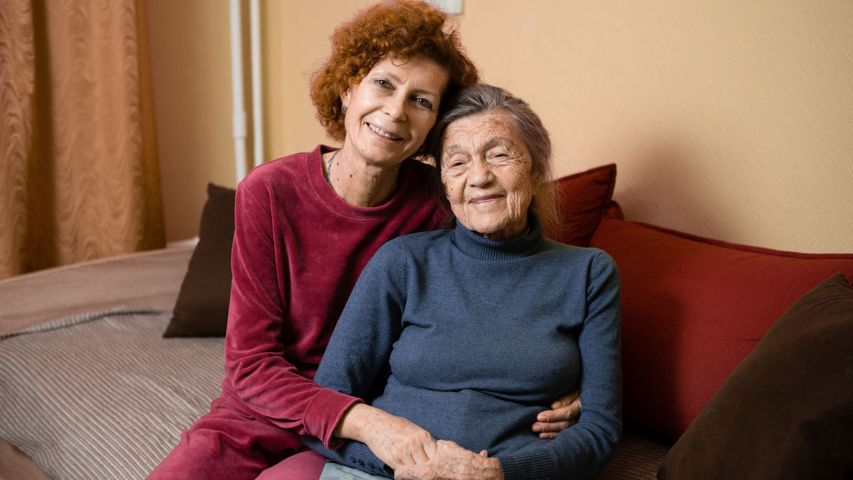 Pensionistin und Tochter sitzen nebeneinander Arm in Arm