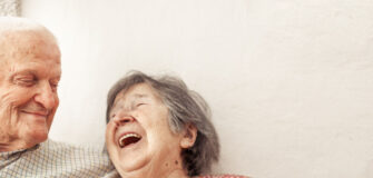 Pensionist und Pensionistin sitzen nebeneinander und lachen zusammen