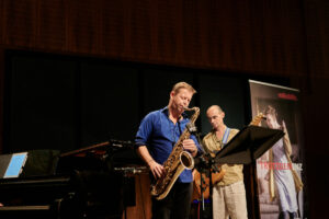 Das Bern Fröhlich Trio spielt auf der Bühne, bestehend aus einem Gitarrist, Saxophonist und Pianist