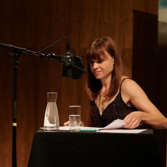 Erwin Steinhauer und Mari Lang sitzen auf der Bühne, haben ihre Mikrofone vor sich aufgebaut und schauen in ihre Unterlagen