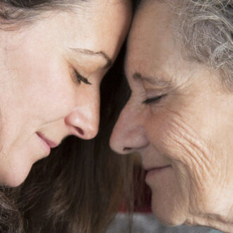Pensionistin und Tochter lehnen ihre Stirn gegeneinander und haben ihre Augen geschlossen und lächeln