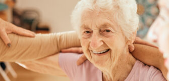 Eine ältere Frau lächelt, arm in arm mit Teilnehmer*innen eines Kurses.