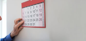 ältere Mann orientiert sich an einem großen Kalender an der Wand.
